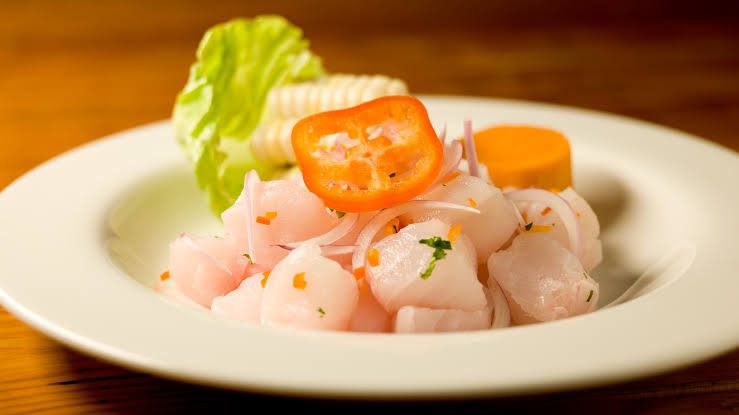 Ceviche peruano servido em prato branco, com cebola roxa, milho e pimenta