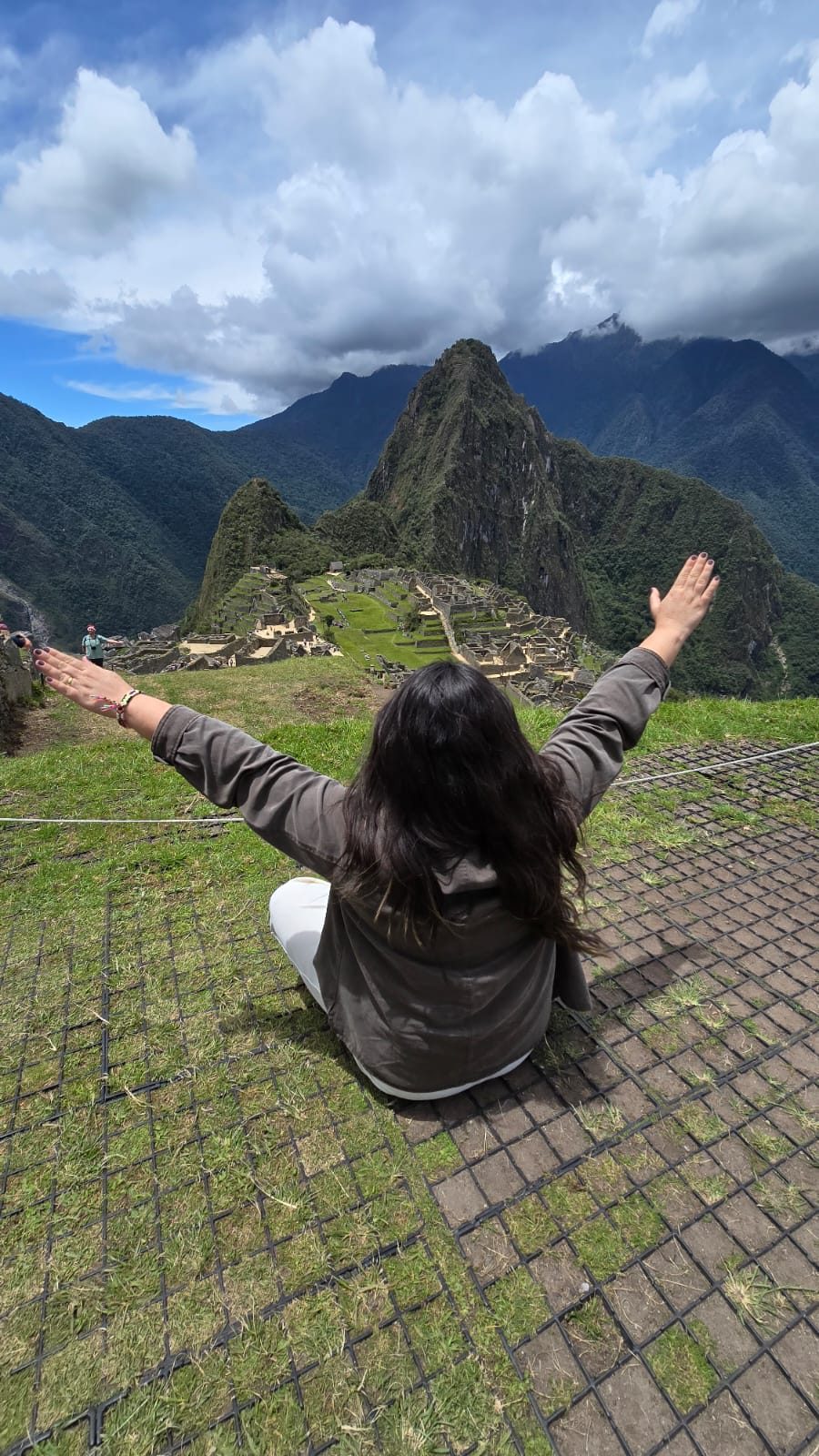 Viajante sentada de braços abertos diante da cidadela de Machu Picchu