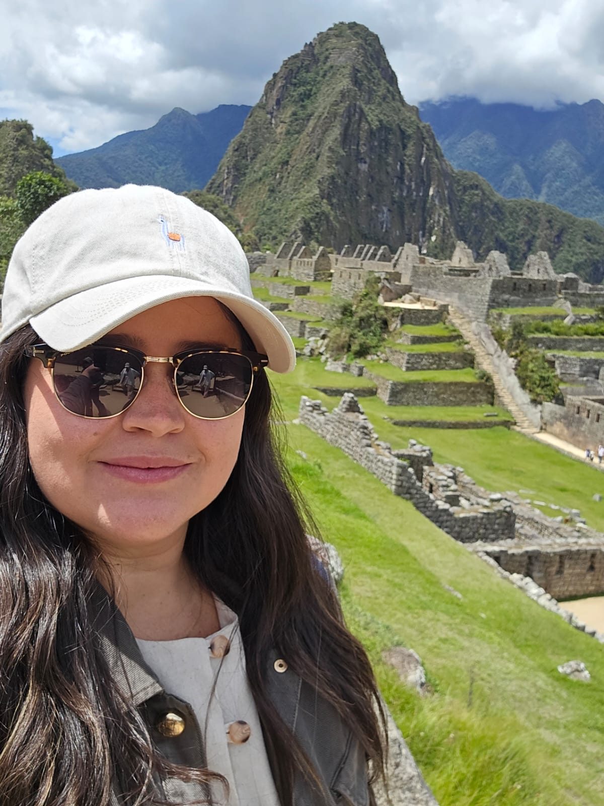 Aline Matos sorrindo diante da cidadela de Machu Picchu